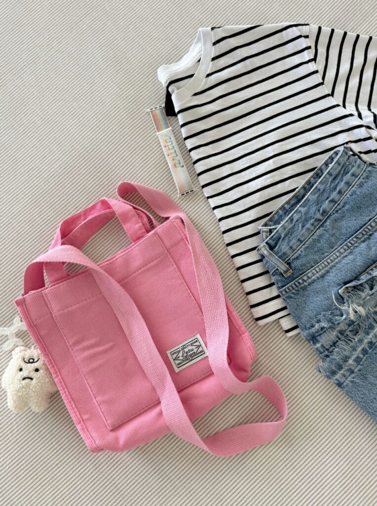 a striped tshirt, blue jeans, pink bag, and lip balm on bed