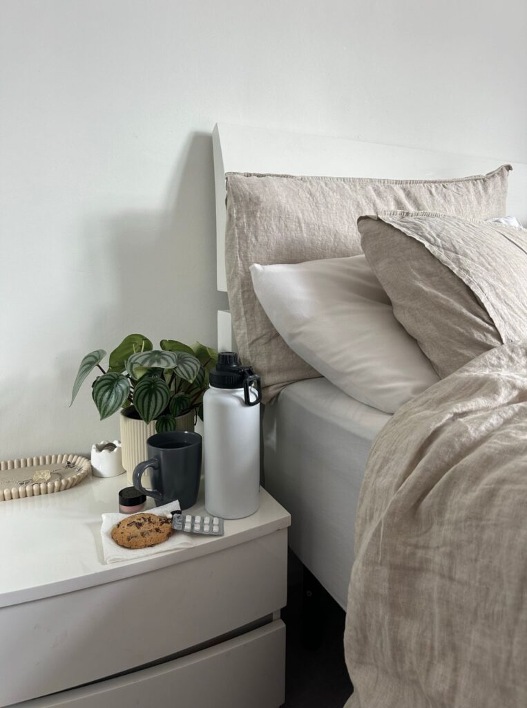 bedside table with bottle, mug, coookies, plant, and meds