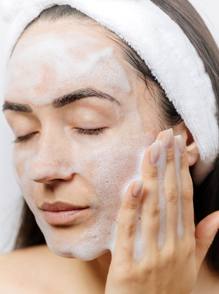 woman wearing headband cleansing her face with foaming face wash