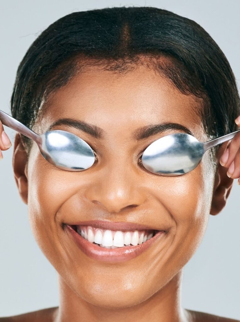 smiling woman pressing cold spoons against her eyes