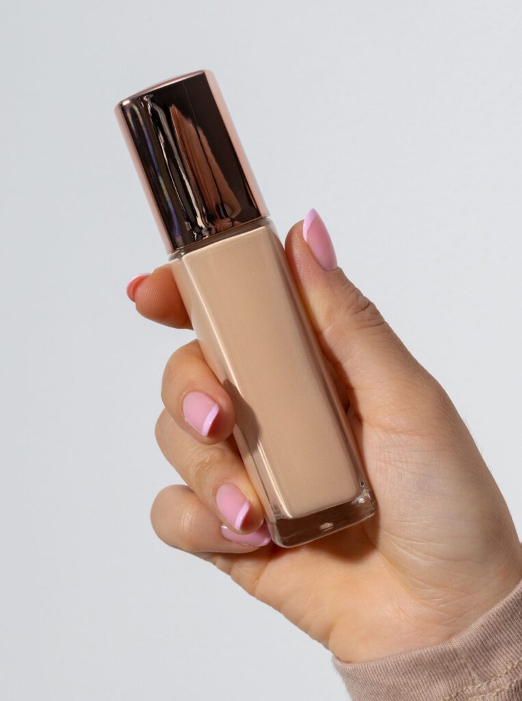 hand with pink nails holding liquid foundation bottle