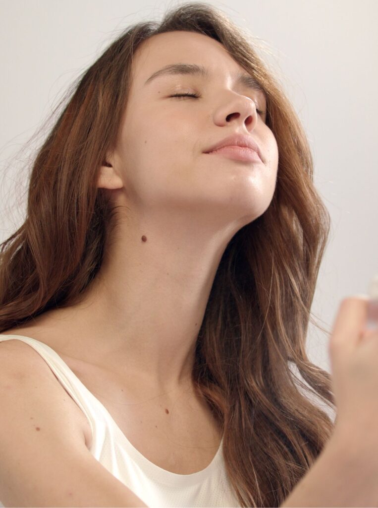 woman putting setting spray on face with eyes closed